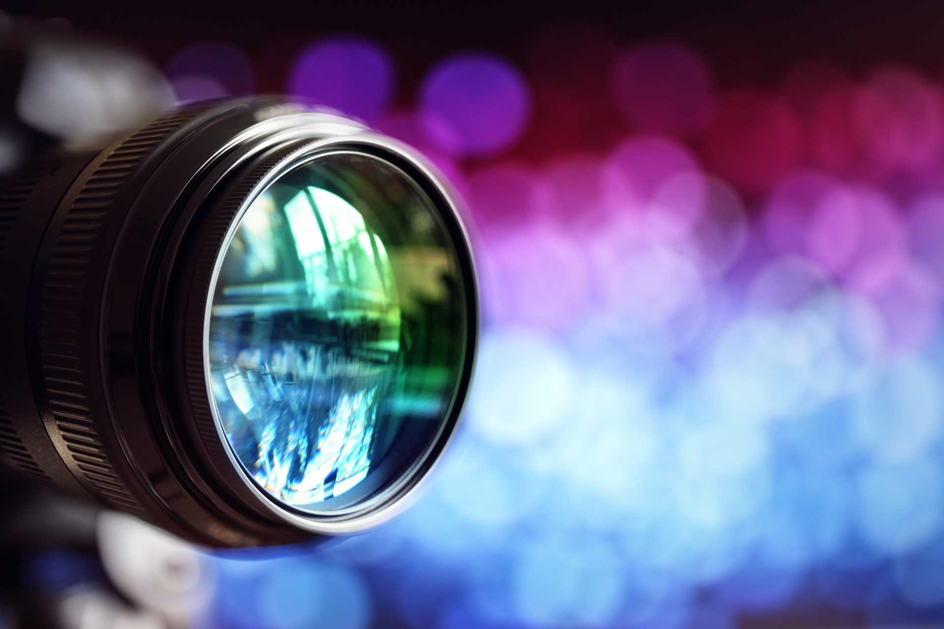 Close-up of a camera lens reflecting the blue and purple lights surrounding it.