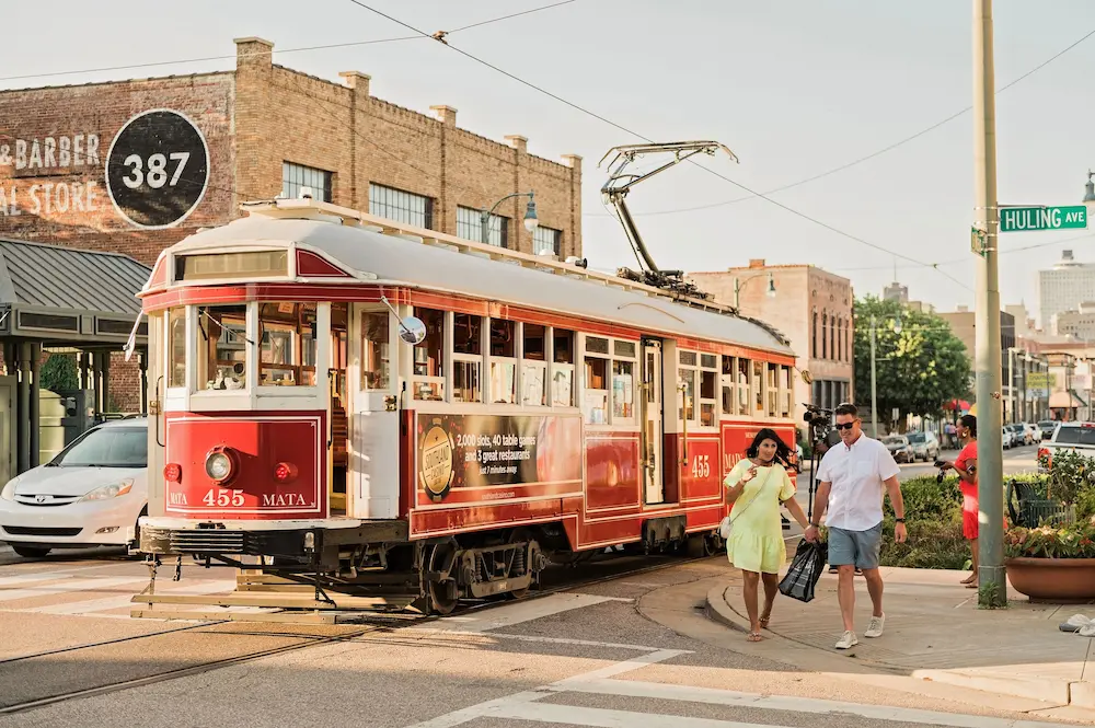 A young couple holding hands and walking in front of a trolley