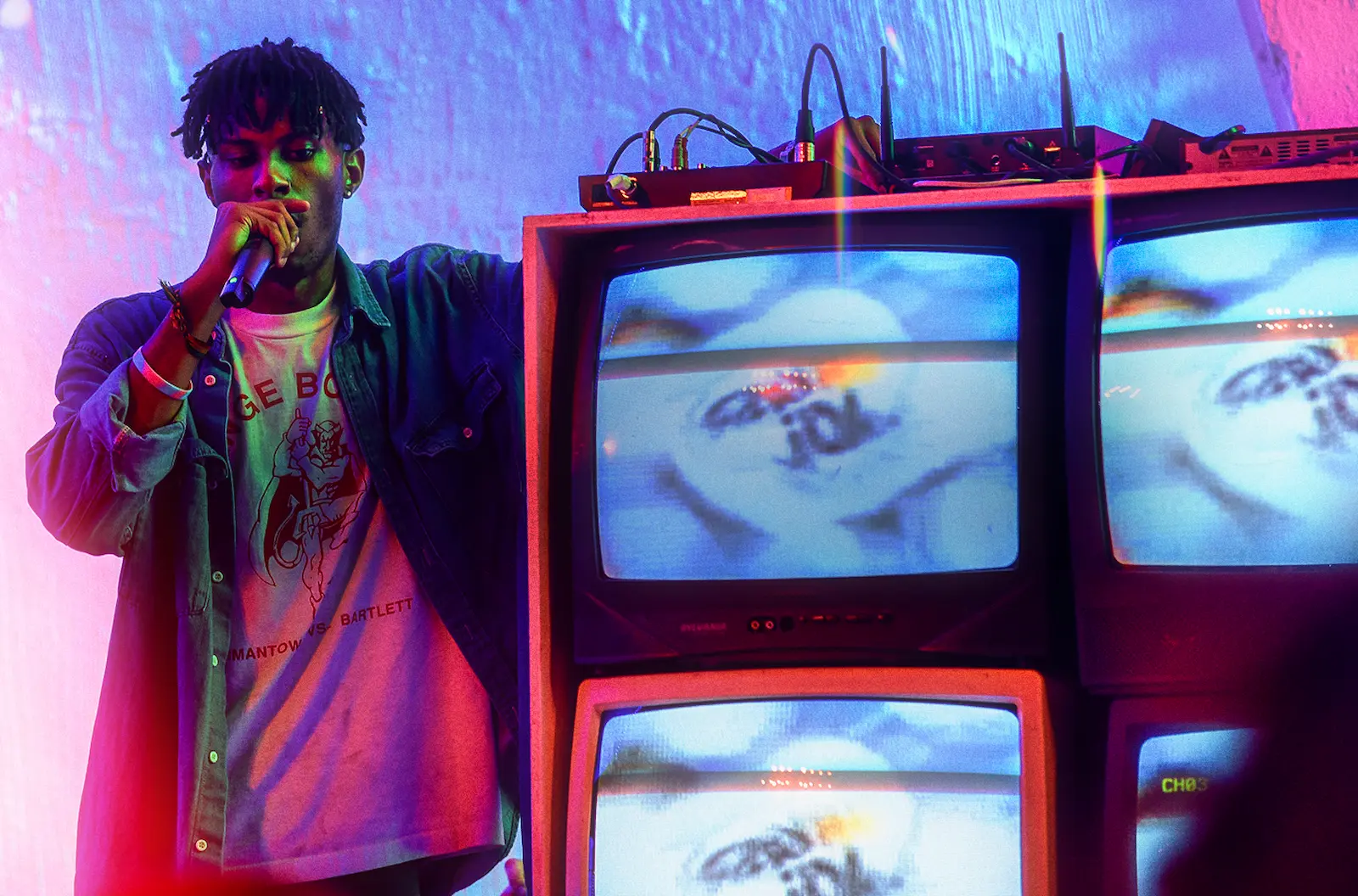 Live Music Artist on stage, standing next to a block of TV's